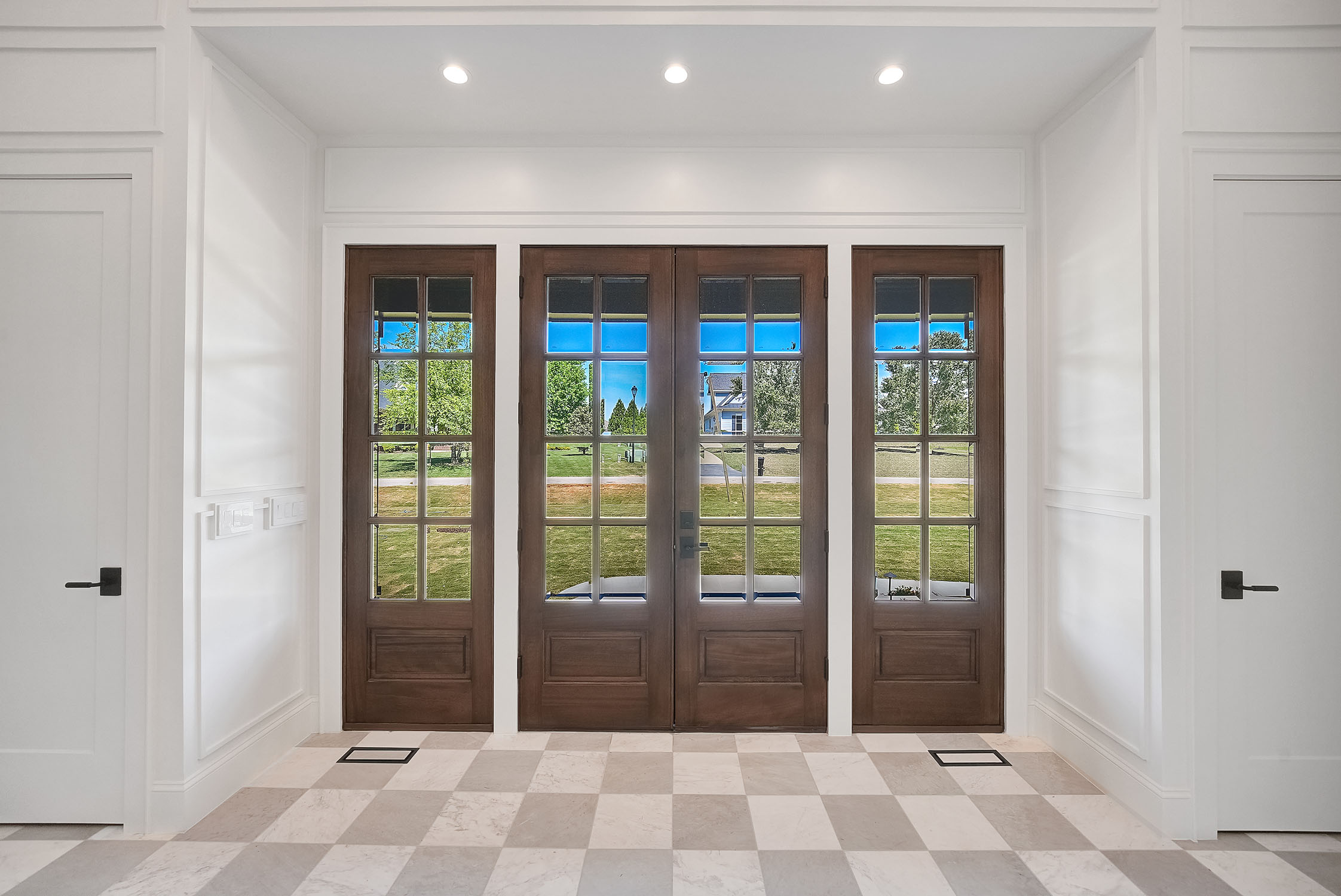 Wooden French doors in bright white foyer