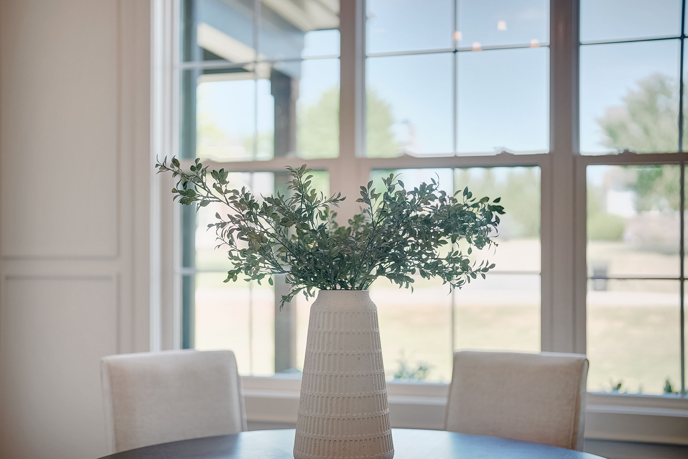 White vase with greenery on dining table