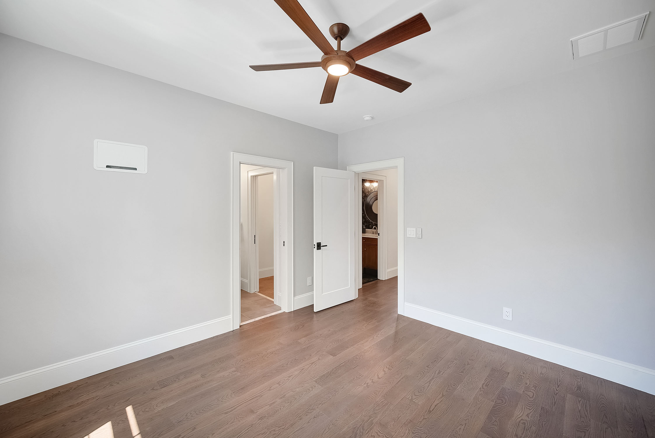 Empty modern bedroom with ceiling fan and hardwood floors