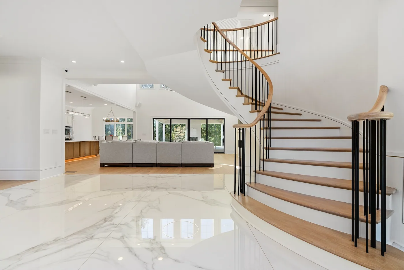 Modern living room with curved staircase and marble floor.